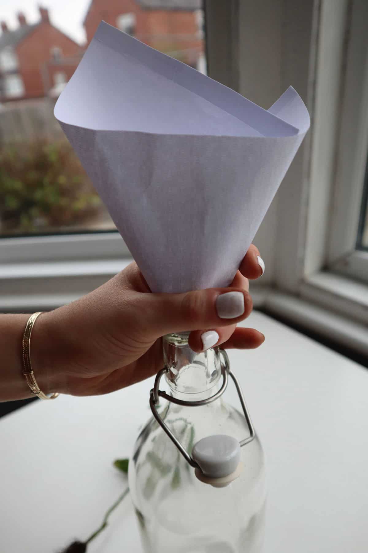 Makeshift funnel with a piece of paper held at the neck of a glass bottle