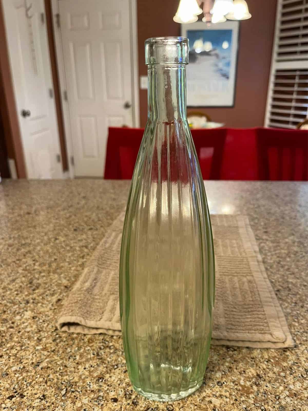 Tall vintage glass bottle with vertical ridges running down on kitchen counter.